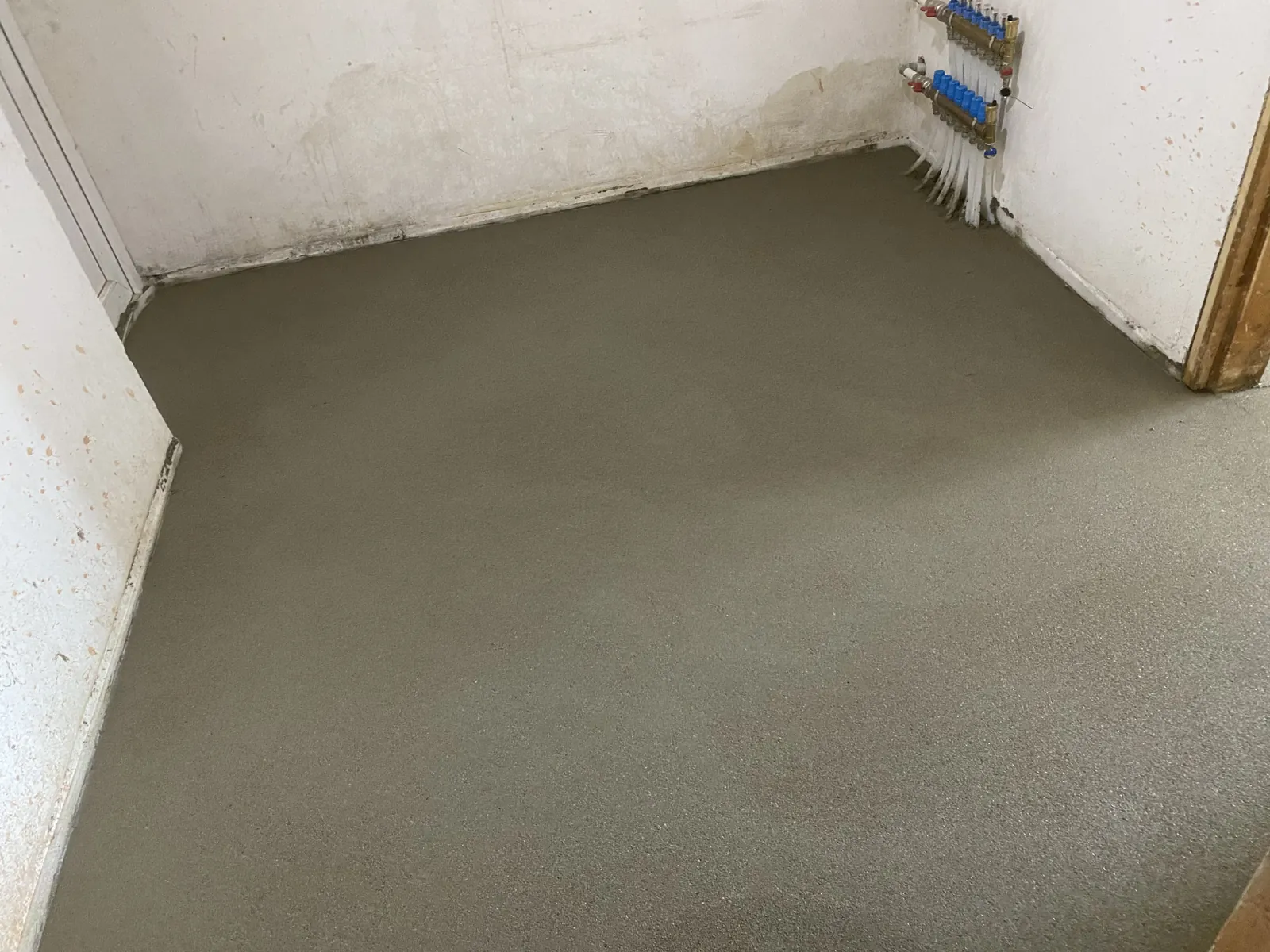 Ką tik išlietos smėlbetonio grindys kambaryje su grindinio šildymo kolektoriumi
